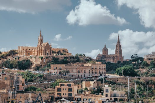 Majestic historic churches set against a Maltese hillside with scenic sky and clouds.