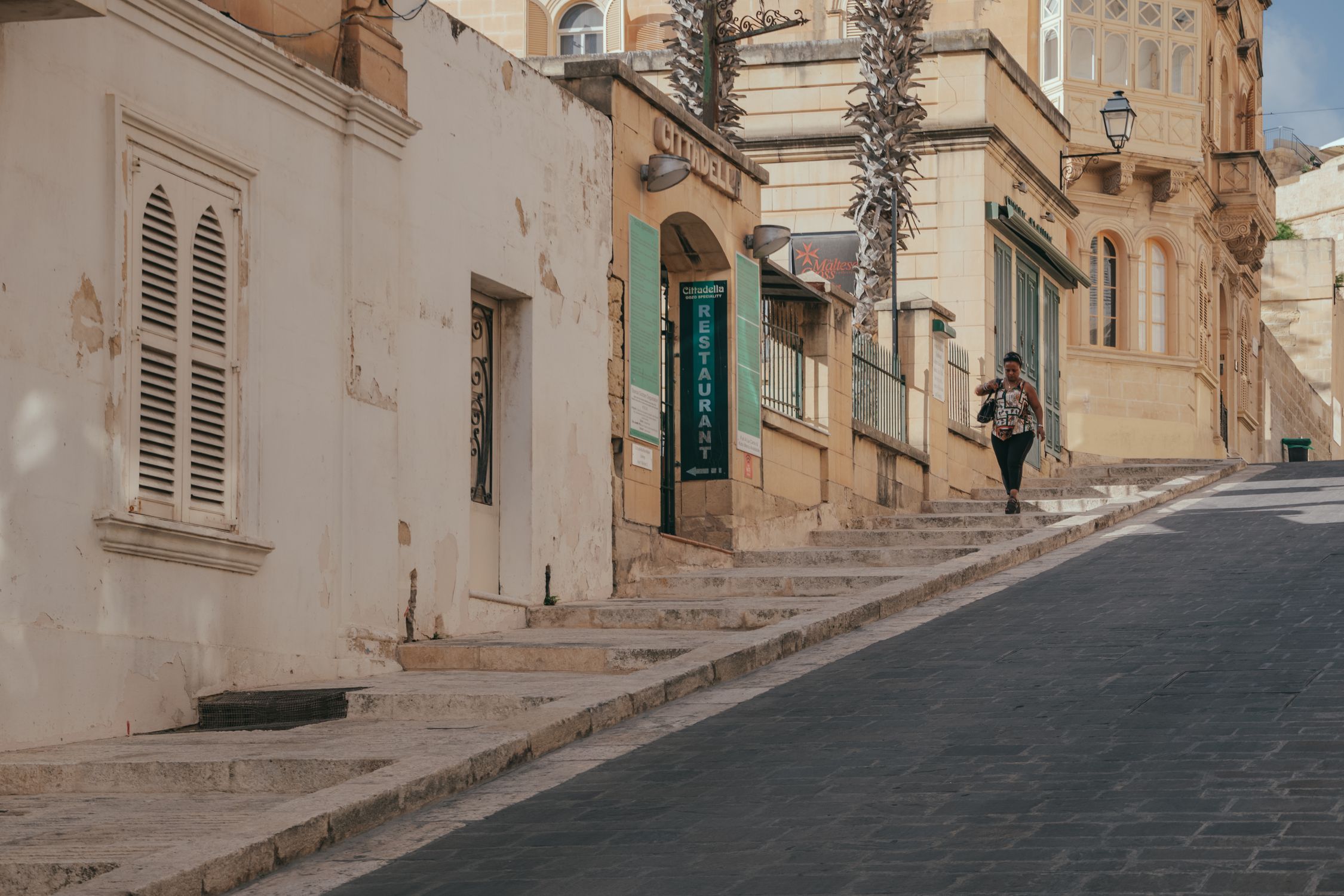 A woman walking along a picturesque street in Victoria, Gozo, Malta under a warm sun.