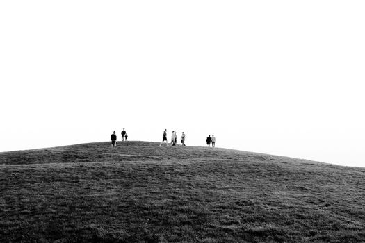 Silhouetted people walking along a grassy hill under a vast sky in black and white.