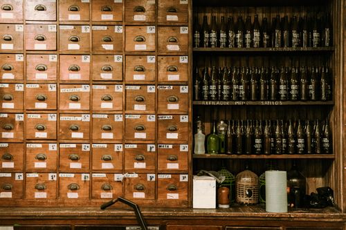 Free A vintage indoor setup featuring wooden drawers and shelves filled with bottles, evoking a nostalgic mood. Stock Photo