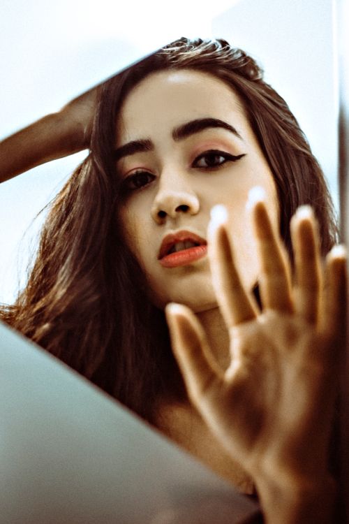 Free A young woman with long hair striking a pose in front of a mirror, creating a captivating reflection. Stock Photo
