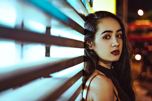 Free A thoughtful woman leans against a wall with urban lights in the background. Stock Photo