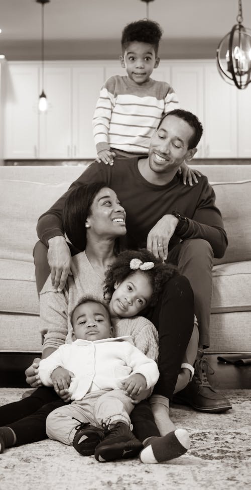 Black and white of smiling African American parents with positive children sitting on sofa in light living room at home