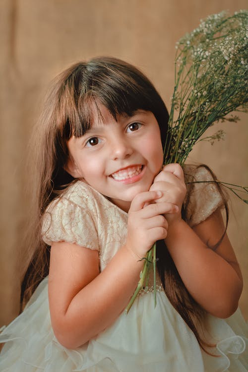 Happy funny little girl with brown eyes smiling and looking at camera on beige background
