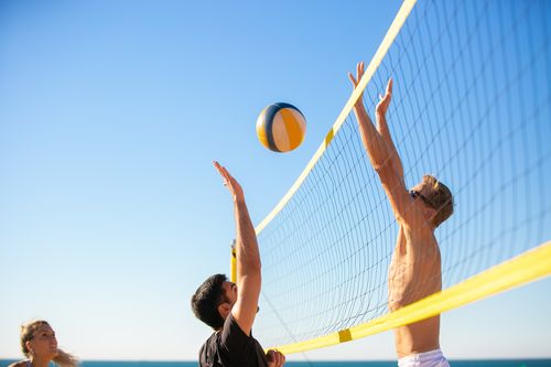 Free Energetic beach volleyball game with players jumping to spike the ball under a clear blue sky. Stock Photo