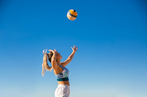 無料 中に青い空の下で黄色と白のバレーボールを保持している白いショートパンツと白いシャツの女性 写真素材