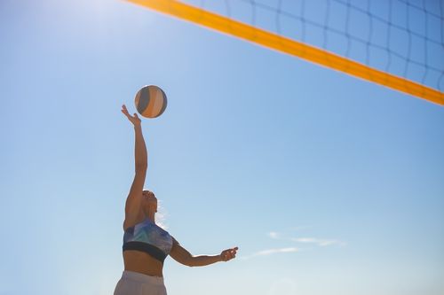 Free A woman spiking a volleyball on a sunny beach with a clear blue sky. Stock Photo