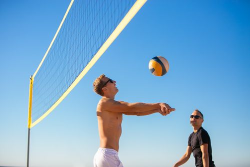 Free Men playing volleyball on a sunny beach with a clear blue sky backdrop. Stock Photo