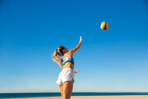 Free A woman expertly spikes a volleyball on a sunny beach day, showcasing athleticism and summer joy. Stock Photo