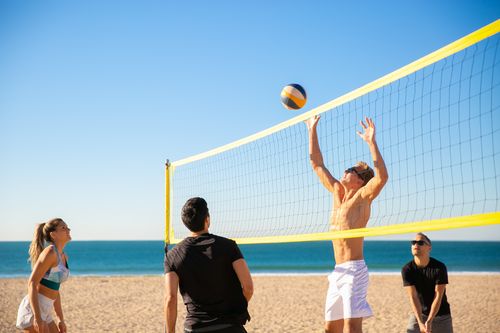 Free Group playing beach volleyball on a sunny day with blue sky and ocean in the background. Stock Photo