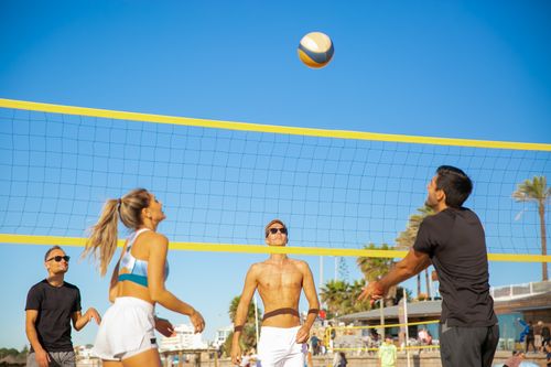 Free Four people actively play volleyball on a sunny beach day, showcasing teamwork and energy. Stock Photo