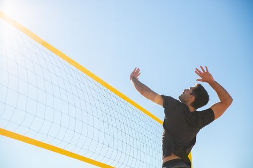 Free Man playing volleyball, jumping for a spike against a clear blue sky, showcasing athleticism. Stock Photo