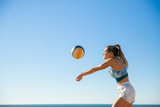 Active woman playing beach volleyball under clear blue sky during daytime.