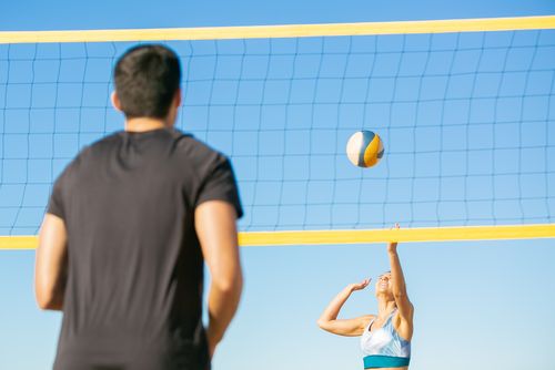 Free A man and woman playing volleyball on the beach under a clear blue sky. Stock Photo