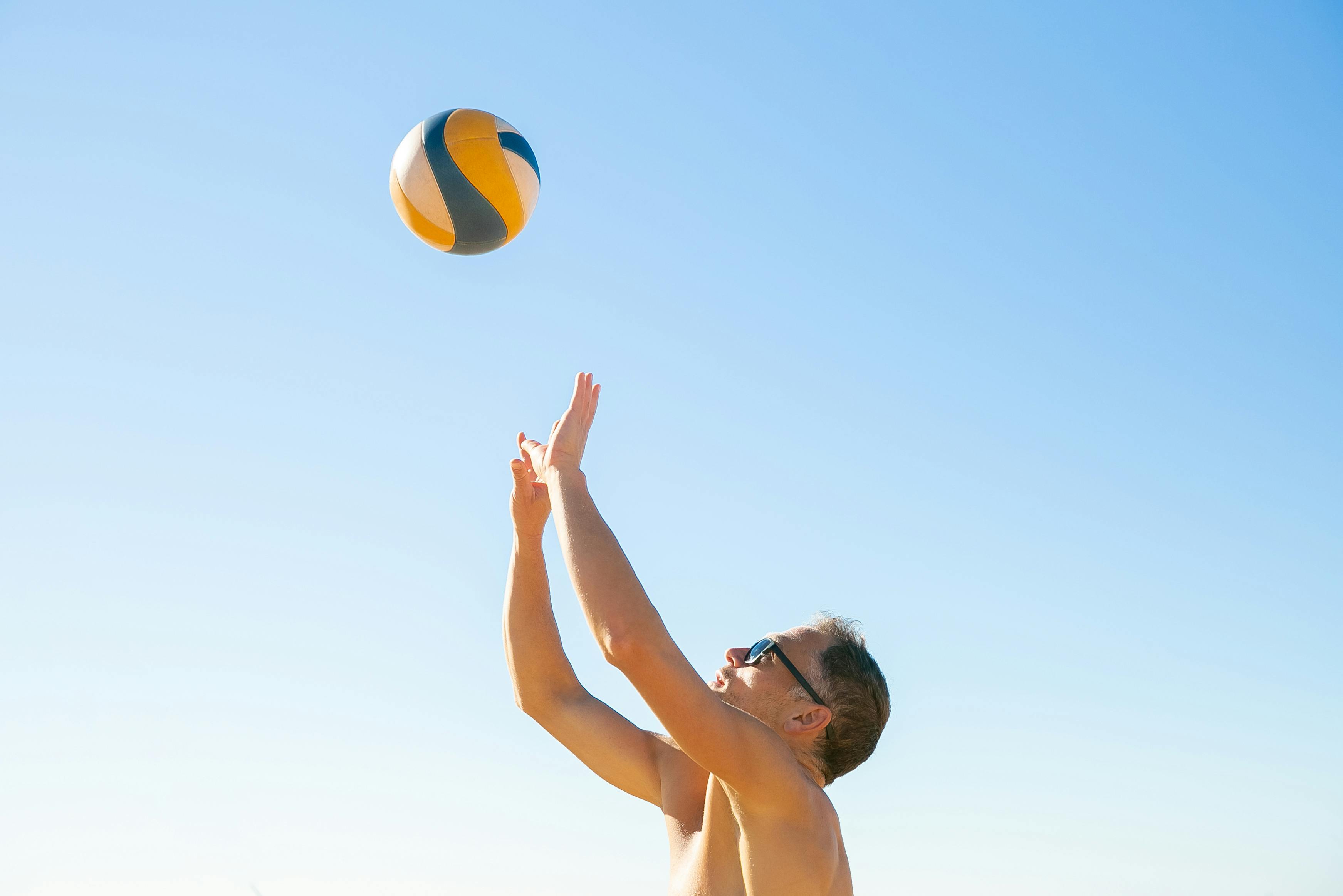 Man playing beach volleyball under a blue sky, showcasing athleticism and outdoor leisure.