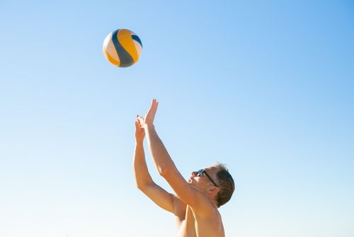 Free Man playing beach volleyball under a blue sky, showcasing athleticism and outdoor leisure. Stock Photo