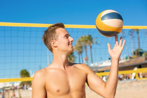 Free Shirtless man playing beach volleyball under a clear sky, showcasing a joyful expression. Stock Photo