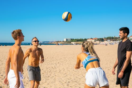 Free Four friends enjoy a game of volleyball on a sunny beach, showcasing teamwork and fun. Stock Photo