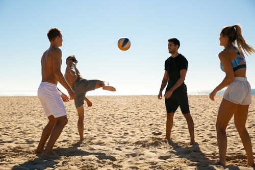 Free Four adults enjoying a game of beach volleyball under a clear blue sky. Stock Photo
