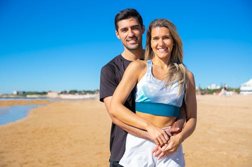 黑色襯衫的男人擁抱女人在棕色沙灘上的藍色背心