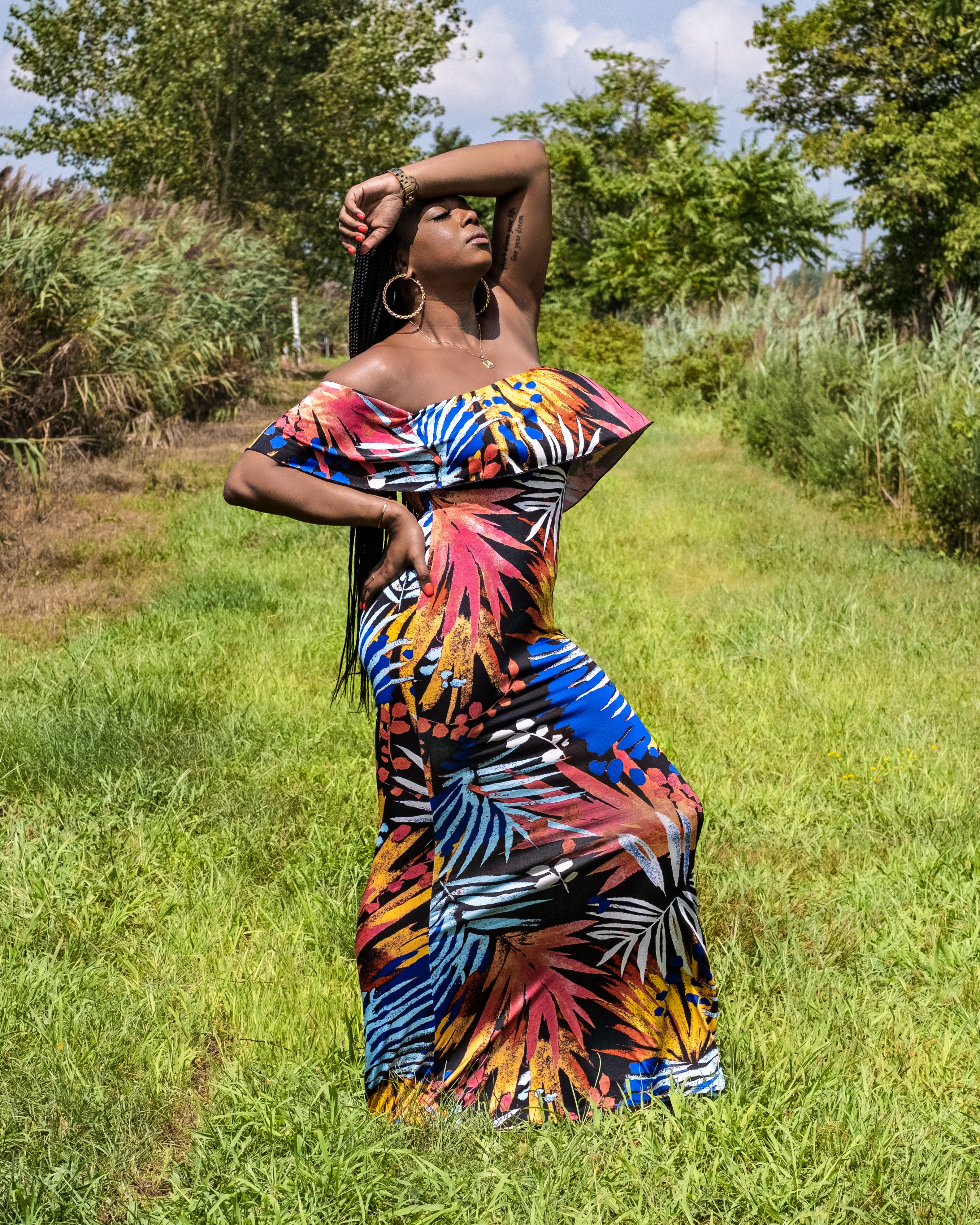 Elegant woman in a vibrant floral dress striking a pose outdoors in a lush green setting.