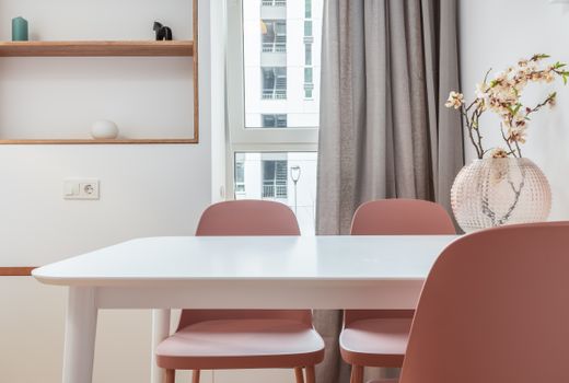 White dining table with chairs in interior of contemporary room with shelves and window with curtains