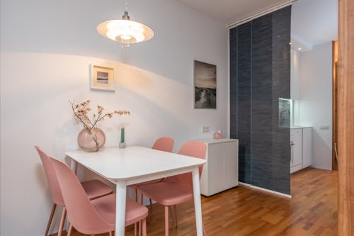 Stylish room with white table with glass vase near pink chairs and painting on wall with light lamp