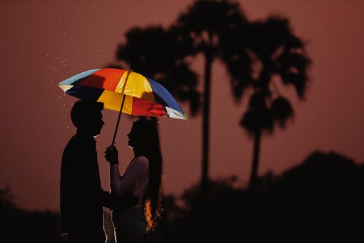 Silhouette of a couple holding a colorful umbrella against a sunset backdrop.