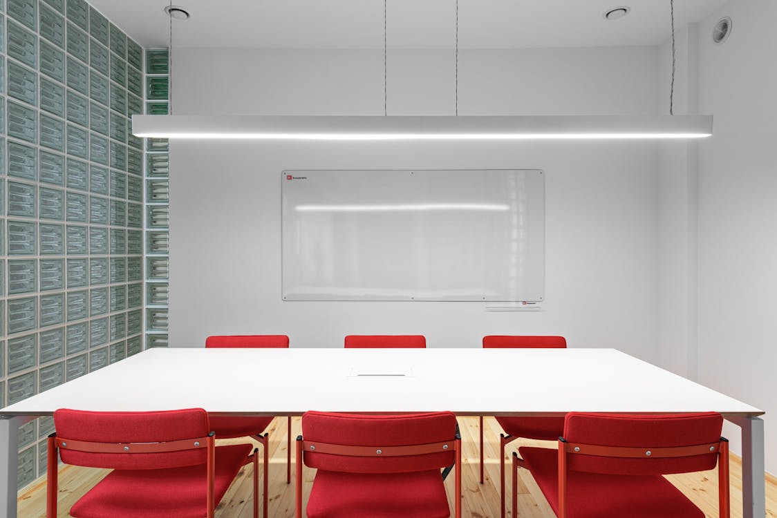 Free Interior of office with white table near red stools and whiteboard on wall near lamp and glass wall Stock Photo