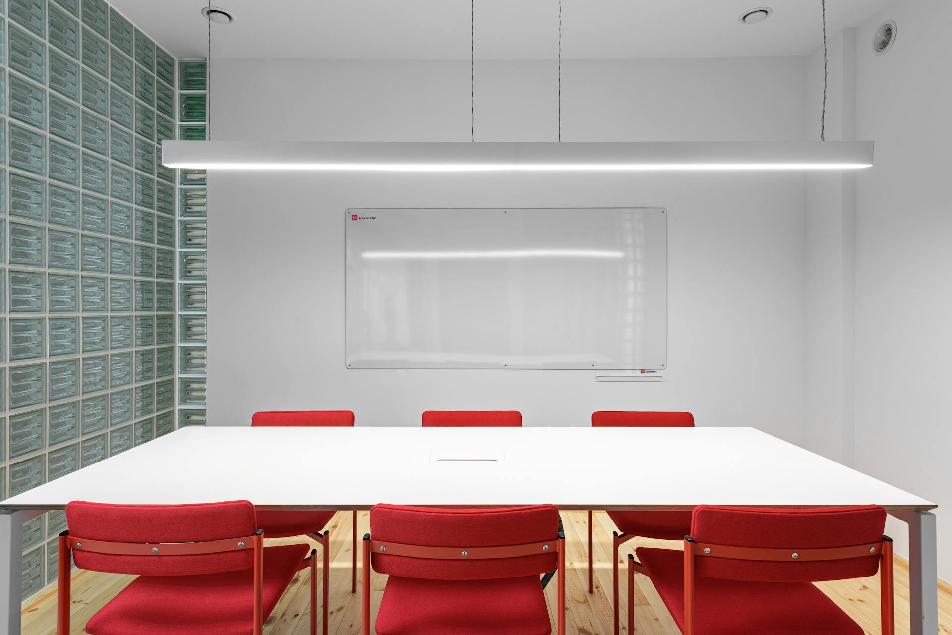 Interior of office with white table near red stools and whiteboard on wall near lamp and glass wall