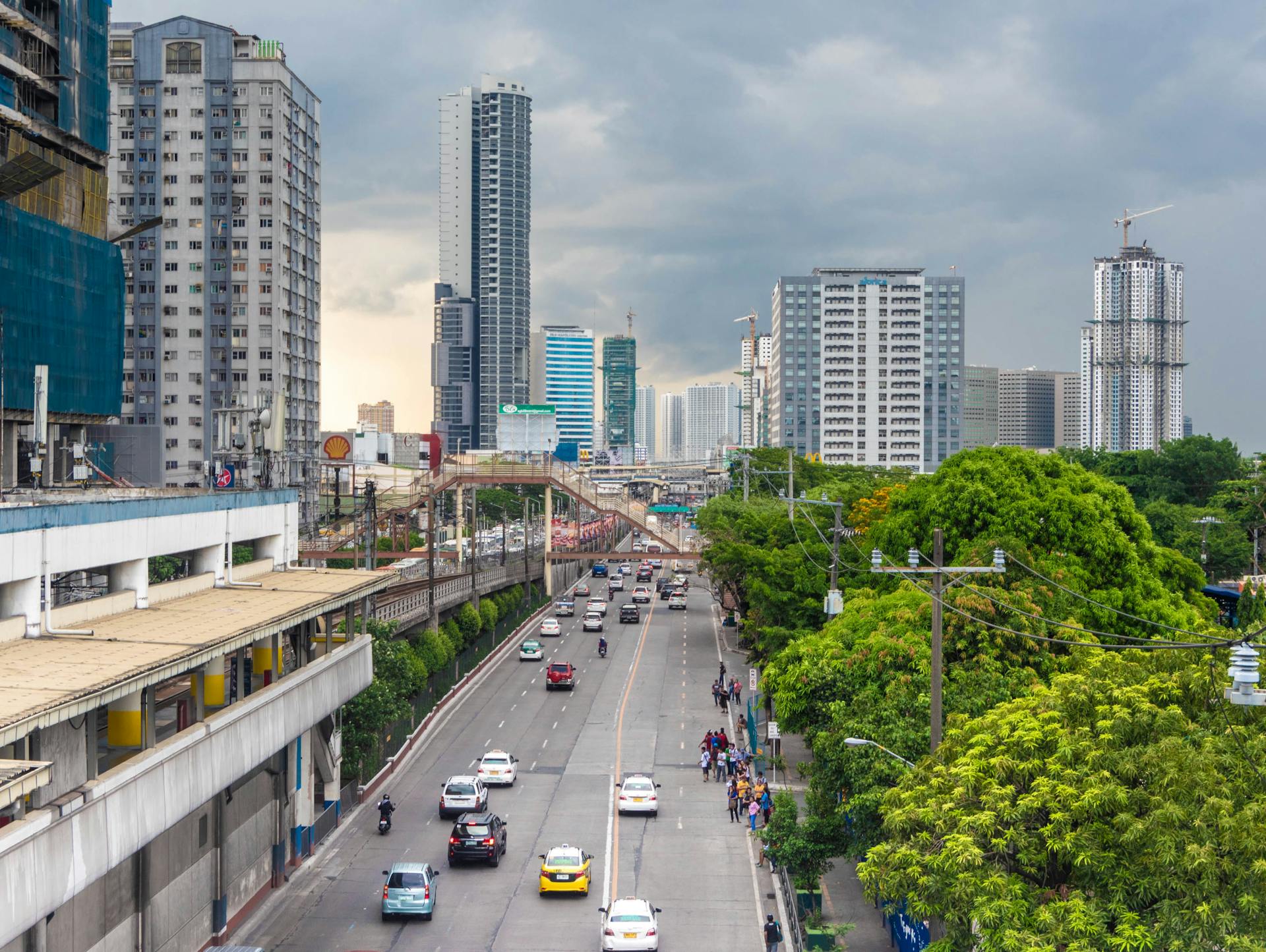 Dynamic cityscape of Manila with skyscrapers, traffic, and greenery under a cloudy sky.
