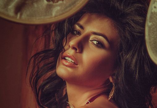 Sensual female with long dark hair standing against red fabric and looking at camera