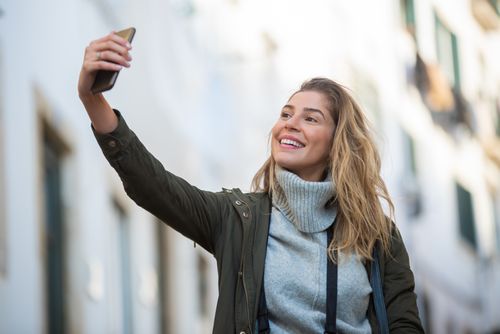 Free Smiling woman takes a selfie on an urban street, capturing a joyful moment outdoors. Stock Photo