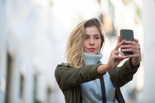 A stylish young woman taking a selfie on a city street during the day.