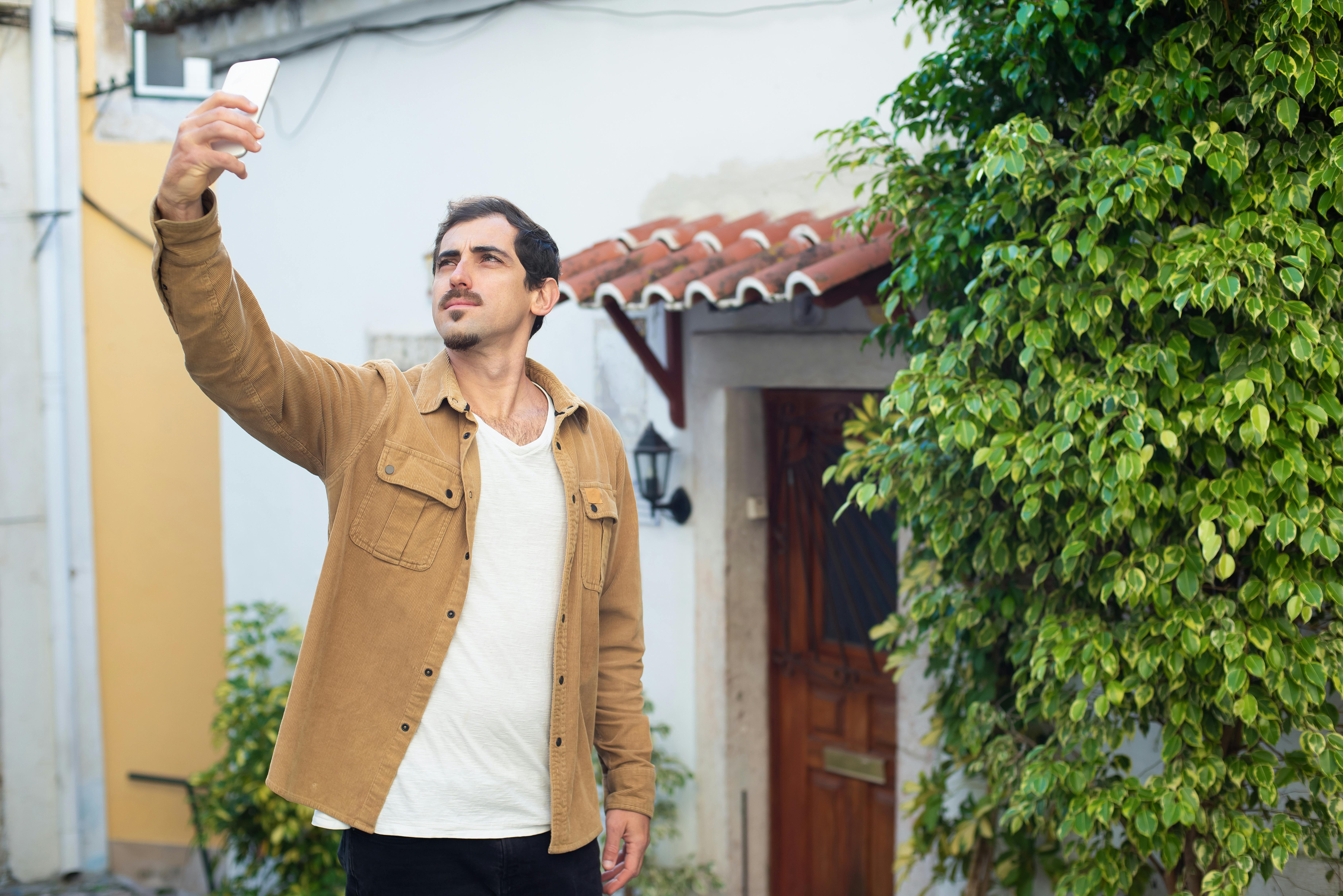 A man in a brown jacket takes a selfie outdoors, capturing travel memories.
