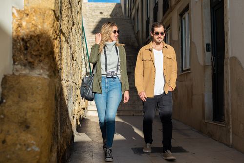 Free A happy couple walking down a sunlit narrow street during their travel adventure. Stock Photo