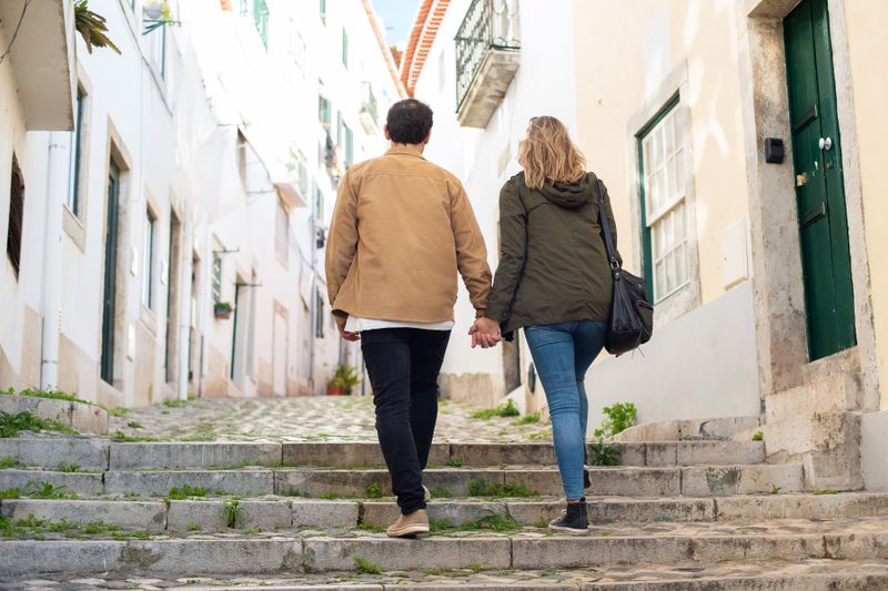 Couple holding hands while walking up cobblestone stairs in a picturesque European alley.