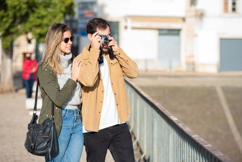 Free A man and woman enjoying a sunny day, capturing memories on camera in an urban setting. Stock Photo