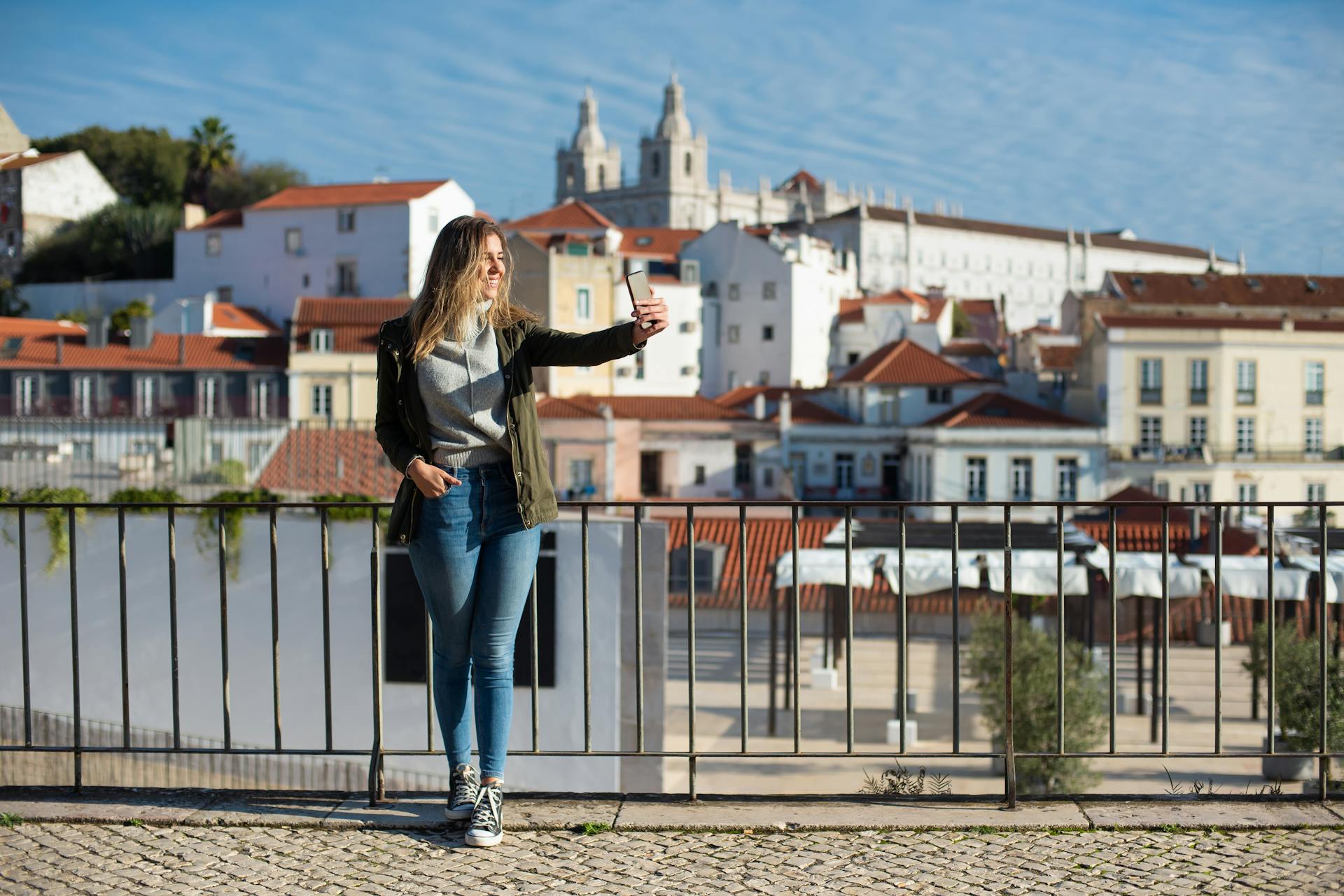A woman takes a selfie with the scenic backdrop of Lisbon architecture.