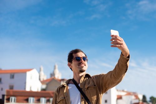 Free Confident man wearing sunglasses capturing a selfie with clear blue sky background. Stock Photo