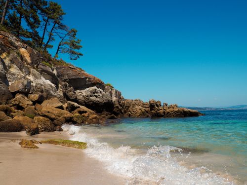 Free Tranquil beach with rocky cliffs and clear turquoise water under a bright blue sky. Stock Photo