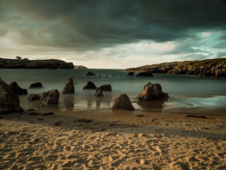 A tranquil beach landscape with rugged rock formations at sunset, reflecting a moody sky.