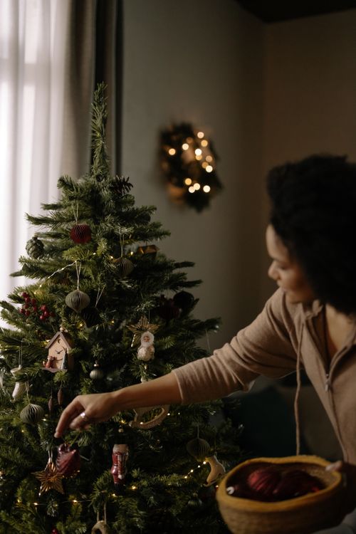 Free A woman decorates a Christmas tree indoors, capturing the cozy Christmas atmosphere. Stock Photo