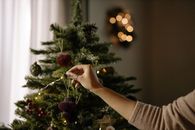 A hand decorates a Christmas tree with ornaments in a cozy indoor setting, evoking holiday cheer.