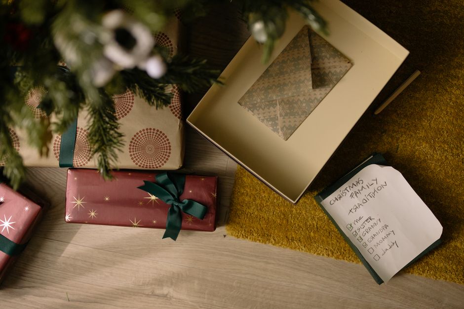 Top view of wrapped Christmas gifts and family checklist under a tree.