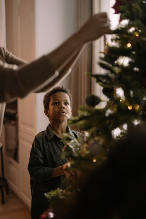 Free Young boy enjoying Christmastime by decorating the tree with family. Stock Photo