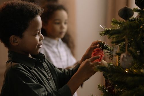 Free Two children decorate a Christmas tree with ornaments, creating a festive holiday atmosphere. Stock Photo