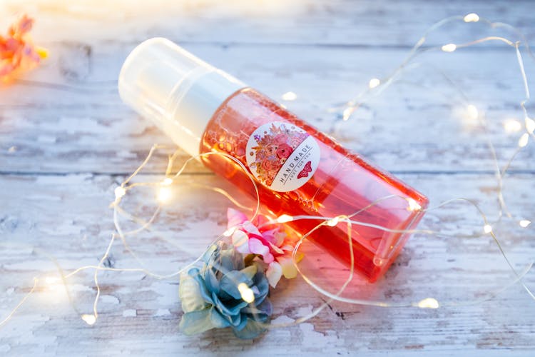 Skincare Toner Placed On Table With Glowing Garland And Flower Heads