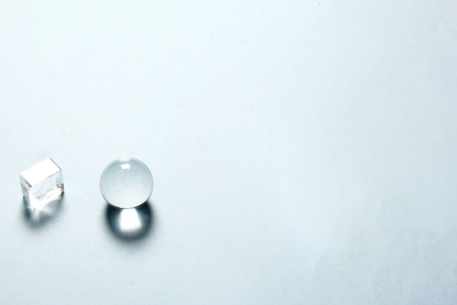 透明なクリスタルの球と立方体が明るい背景に影を落とすミニマリストの構図。