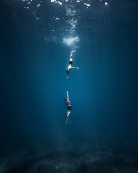 Stunning view of two free divers swimming gracefully underwater in deep blue ocean.